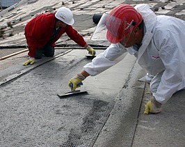  Foto von zwei Personen die mit Spachteln ein Gitter mit Beton bestreichen.