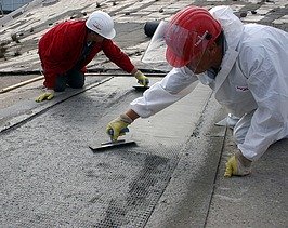  Foto von zwei Personen die mit Spachteln ein Gitter mit Beton bestreichen.