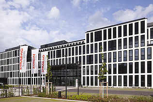 Das Foto zeigt das neue Konzernhaus in Köln, ein modernes Gebäude, fünstöckig mit vielen Feinstern, davor eine Grünfläche