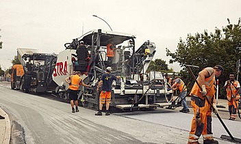 Foto von mehreren Straßenbauarbeitern rund um eine große Asphaltbaumaschine