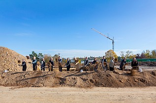 Foto von mehreren Männern auf einer Baustelle die mit einen Sparten Erde in die Luft werfen. 