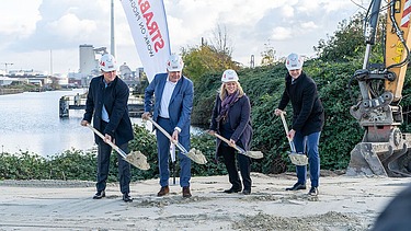 Foto von vier Personen mit Schaufeln, die einen Spatenstich durchführen, dahinter ein STRABAG Segelbanner