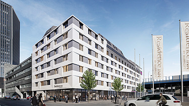 Foto von einem weißen, modernen Eckhauses, davor ein Parkplatz und zwei weiße Fahnen rechts