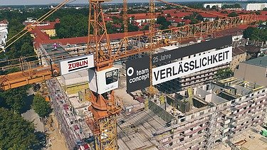 Foto von einem Kran auf einer Baustelle der ein Banner trägt.  