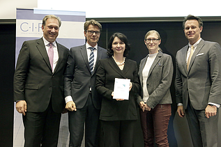 Photo of several people standing, the person in the middle holding a certificate