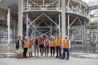 Foto von mehreren Personen, vor einem Gerüst, in Schutzausrüstung. 