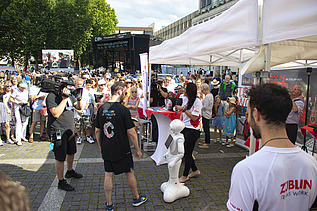 Foto von einem ZÜBLIN-Stand, wo ein Roboter gefilmt wird. Drumherum sind viele Personen versammelt    