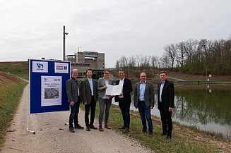 Photo of five people standing on a gravel road, to the left a blue sign