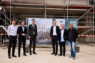 Foto von mehreren schick gekleideten Personen auf einer Baustelle.