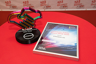 Auf einemTisch mit roter Tischdecke liegt rechts eine Urkunde und links steht ein Flaspokal