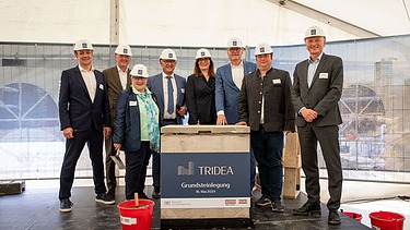 Foto von mehreren schick gekleideten Personen mit Helm vor einem Pult. 