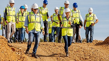 Foto von mehreren Personen in Schutzwesten und Bauhelmen, die auf einem Erdhügel stehen