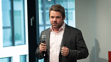 Foto von Klemens Haselsteiner im Anzug mit Microphon in der Hand. 