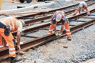 Foto von drei Schienenbauarbeitern beim Schienenverlegen