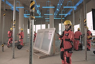 Foto von einer Baustelle in einem Gebäude. Es sind mehrere Personen mit Schutzausrüstung zusehen. Die Decke wird von Stangen getragen.   