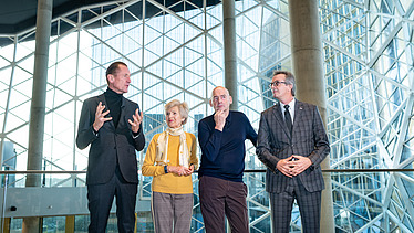 Foto von vier Personen vor einer Glaskuppel, sie schauen nachdenklich.  