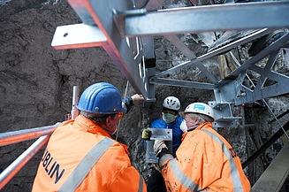 Foto von drei Personen in Schutzuniform und Mund-Nase Maske die an einem Stahlträger arbeiten.     