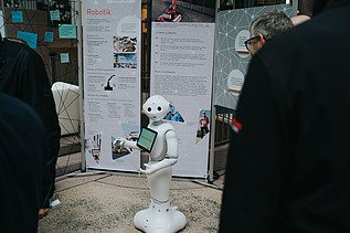 Foto von einem kleinen, weißen Roboter, der vor einem Messestand steht