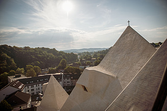  Foto von einer Kirche in einer Stadt, mit Blick von den Dächern der Kirsche. Drumherum ist ein Wald.