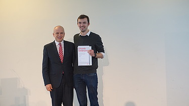 Foto von zwei Personen, die glücken schauen. Ein hält eine Urkunde für einen Sonderpreis in der Hand.      