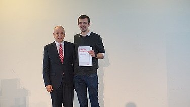 Foto von zwei Personen, die glücken schauen. Ein hält eine Urkunde für einen Sonderpreis in der Hand.      