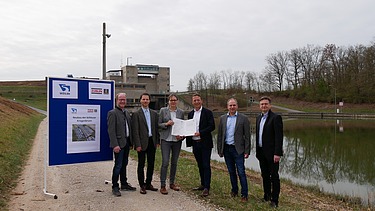 Photo of five people standing on a gravel road, to the left a blue sign
