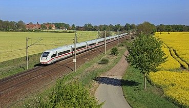 Foto einer Bahnstrecke mit einem weißen Schnellzug, links und rechts blühende, gelbe Rapsfelder