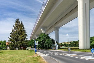 Foto einer neuen Talbrücke von unten gesehen, daneben verläuft eine Landstraße