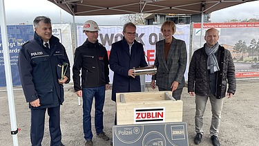 Foto mehreren Personen die eine Röhre in eine Holztruhe legen.   