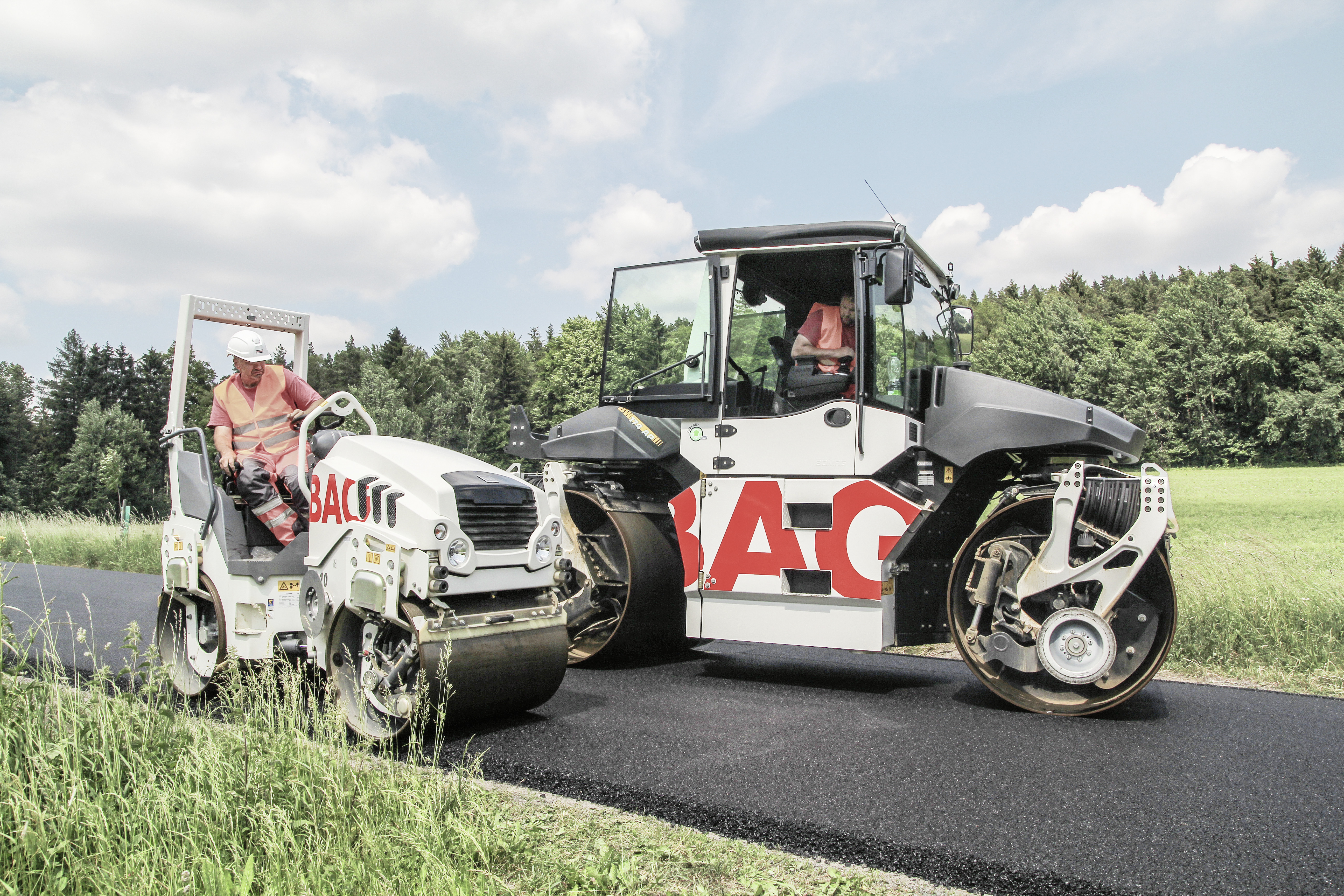 Two construction machines with STRABAG lettering can be seen paving a road after it has been tarred.