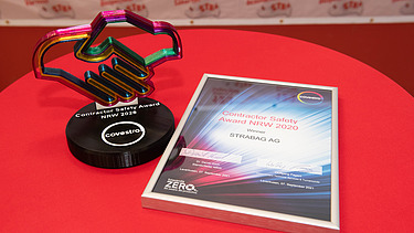 Auf einemTisch mit roter Tischdecke liegt rechts eine Urkunde und links steht ein Flaspokal