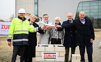 Foto von mehreren Personen, die eine Röhre halten zum Richtfest.  