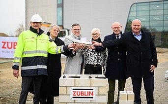 Foto von mehreren Personen, die eine Röhre halten zum Richtfest.  