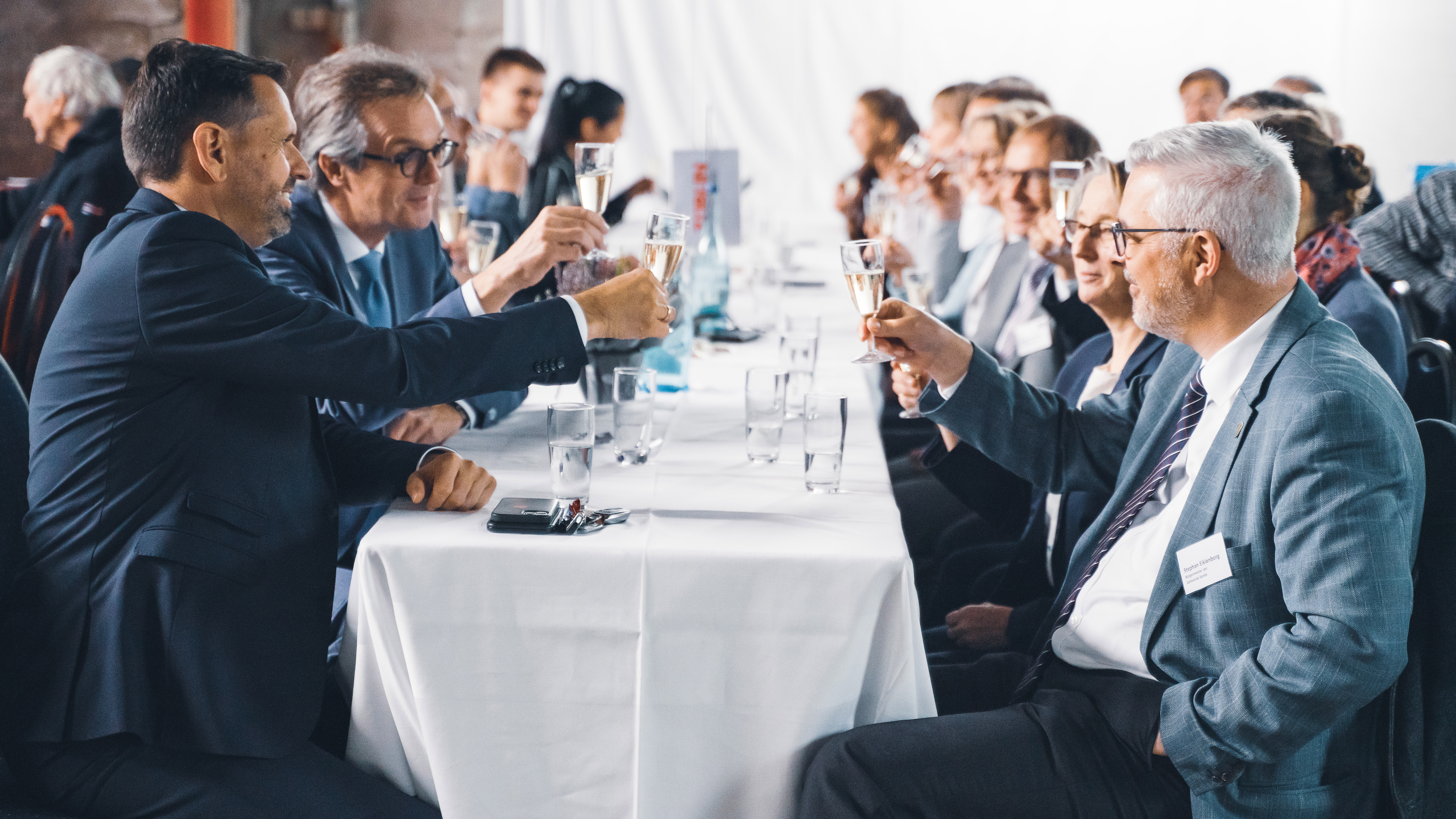 Foto von mehreren Personen bei der Jubiläumsfeier am Standort Sande. Sie sitzen an einem Tisch und stoßen an. 