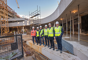 Foto von mehreren Personen mit Bauhelmen und Schutzwesten in einer Baustelle