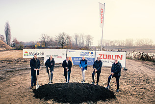 Foto von mehreren Männern, die einem Sparten in die Erde stecken. Sie schauen glücklich. 