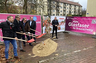 Foto von mehreren Personen beim symbolischen Spatenstich mit Schaufeln in der Hand, dahinter Bautransparente mit der Aufschrift Glasfaser