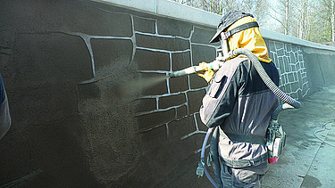  Foto von einer Person, die eine Wand mit brauner Farbe besprüht.