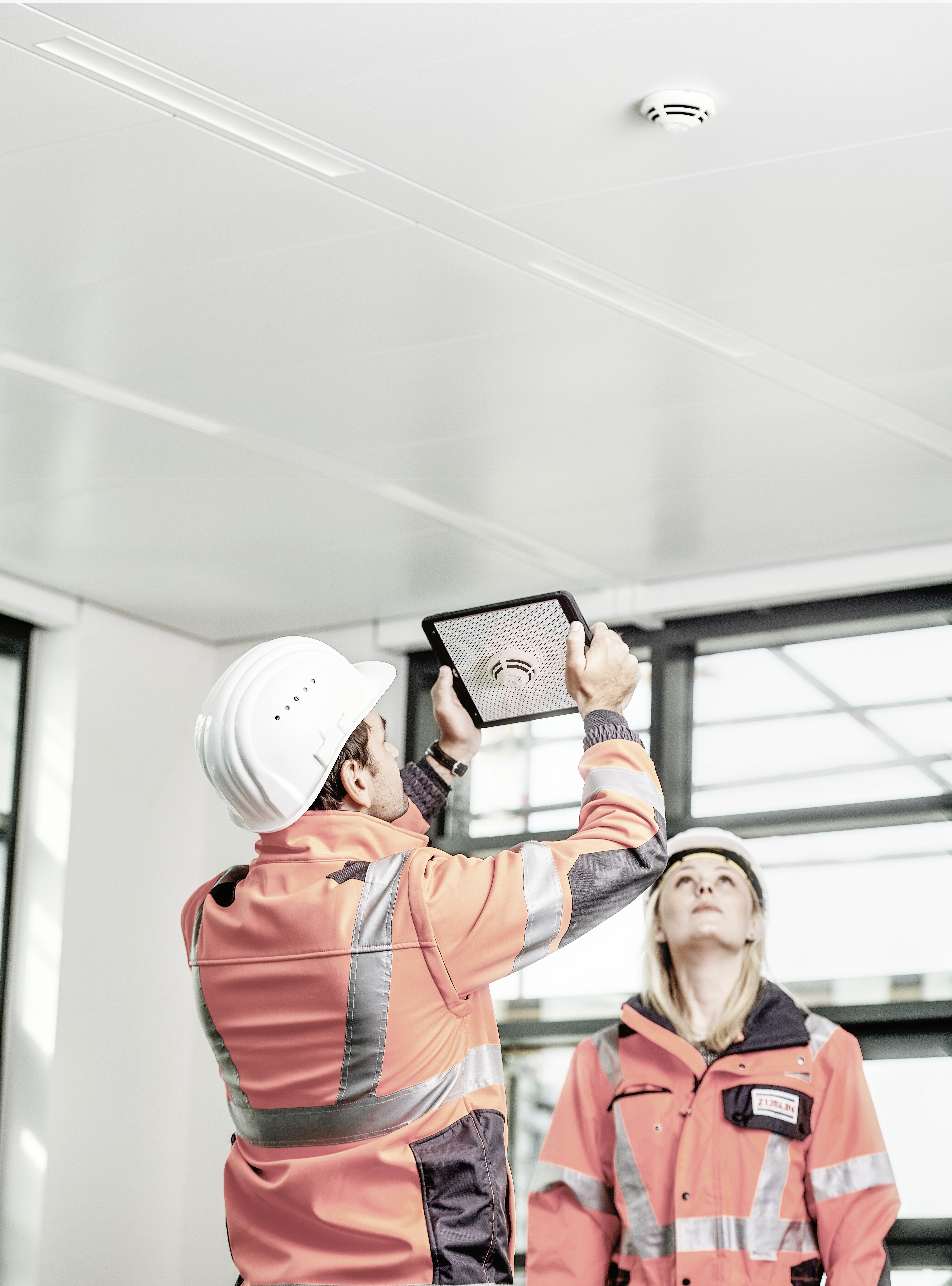 Two STRABAG employees can be seen using a tablet to inspect an object on the ceiling wall.