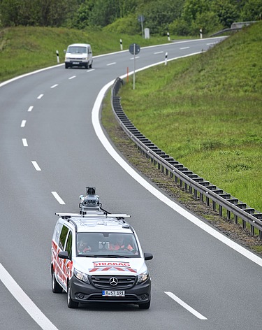 Foto eines Fahrzeuges mit einem Vermessungsgerät auf dem Dach auf einer zweispurigen Fahrbahn
