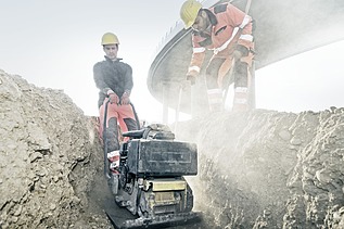 Photo of two construction workers with a machine doing civil engineering work in a trench