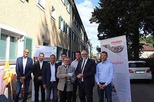 Foto von mehreren Personen, die vor einem gelben Gebäude stehen, hinter ihnen sind zwei Roll-ups