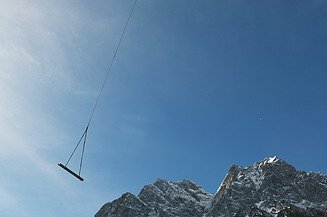 Foto von einem Hubschrauber der Material an einem Seil transportier in einem Gebirge.  