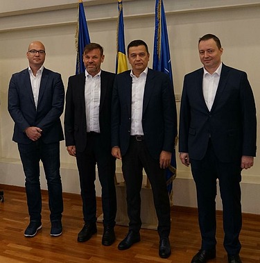 Photo of four people standing in front of three flags