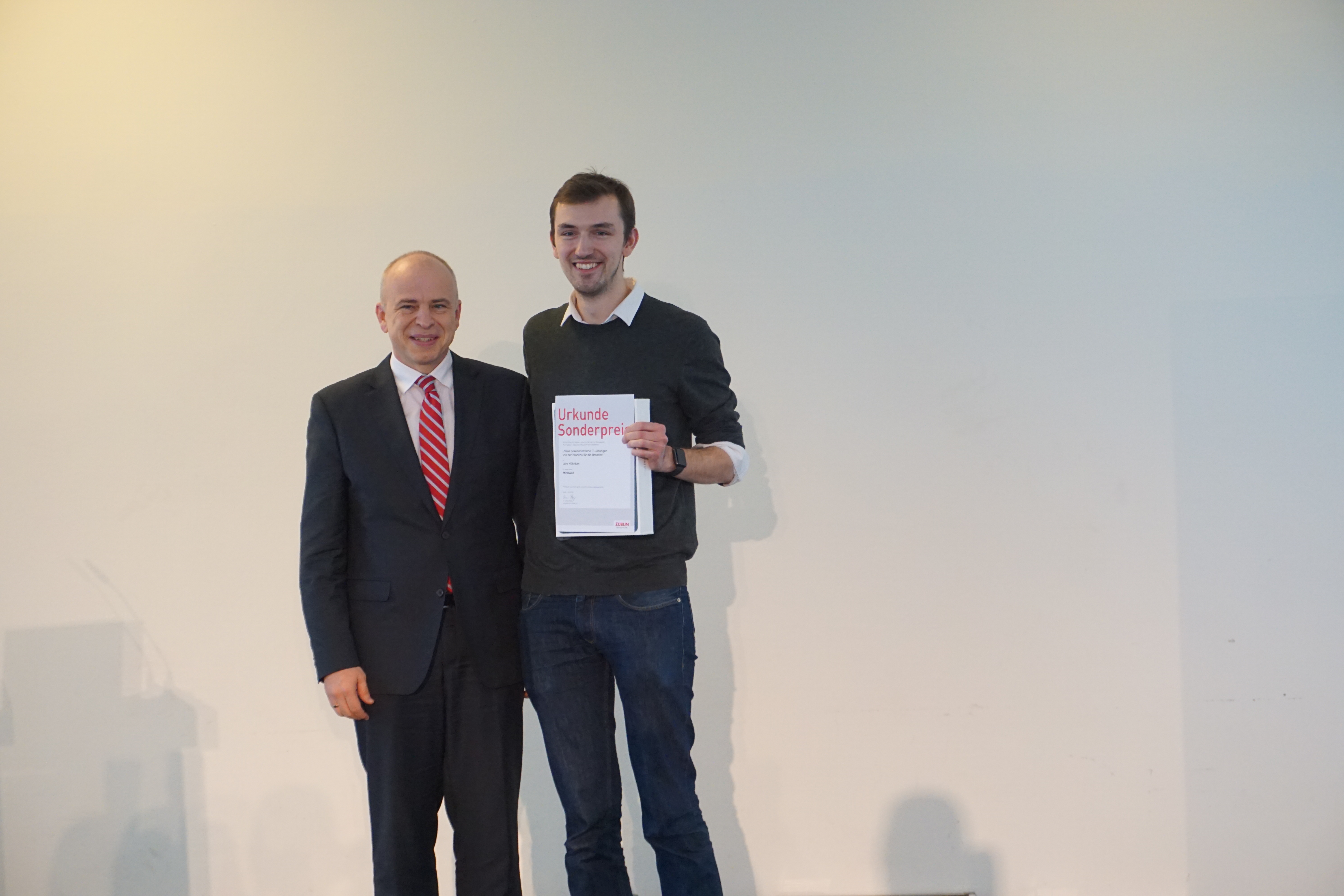 Foto von zwei Personen, die glücken schauen. Ein hält eine Urkunde für einen Sonderpreis in der Hand.      