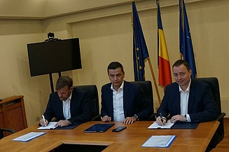 Photo of a contract signing with three people sitting at a table