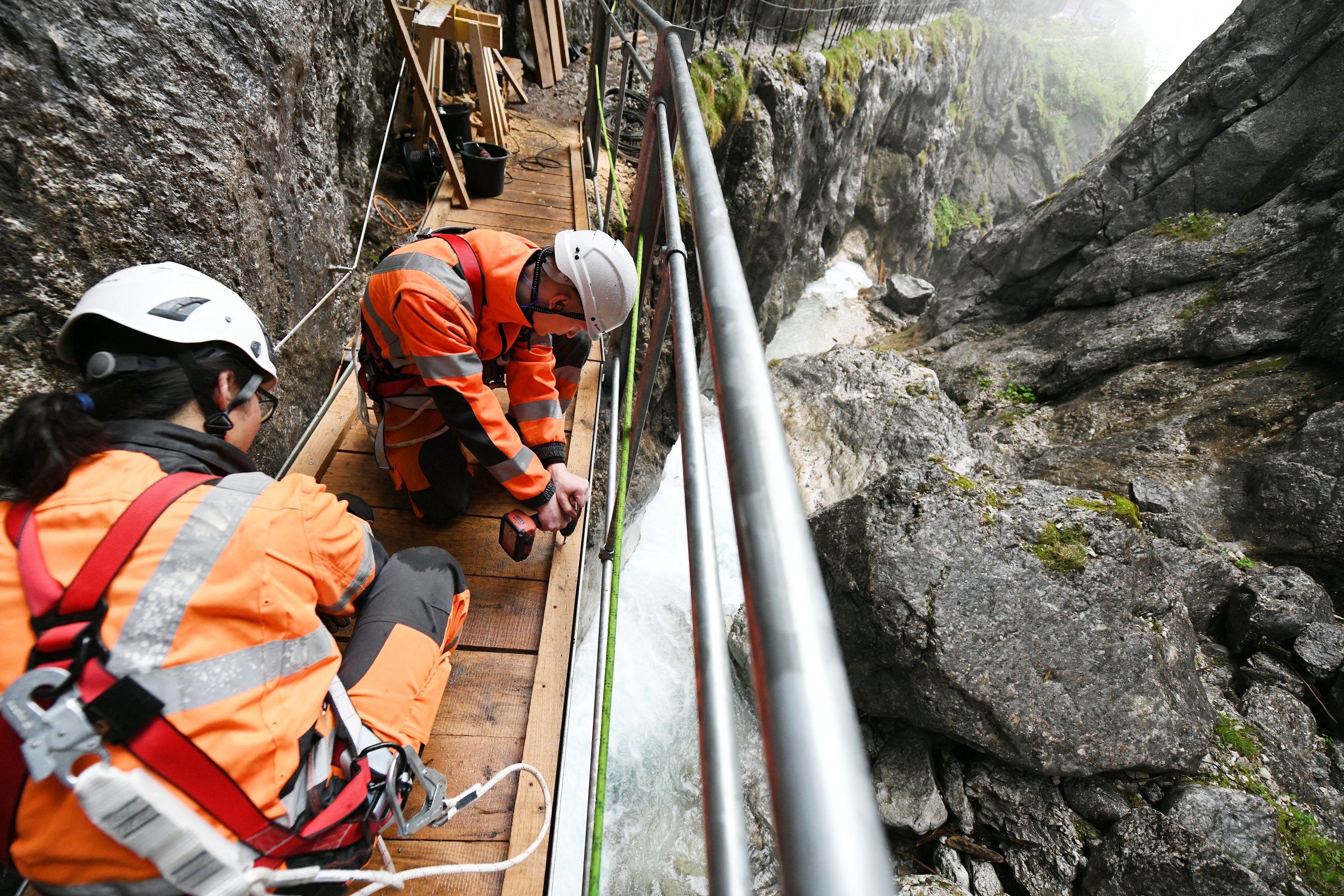 Foto von zwei Personen in Schutzuniform die in einer Schlucht an einer kleinen Brücke schrauben.    