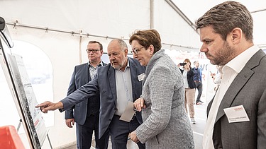 Photo of four people looking at a construction board, the second person from the left pointing at it
