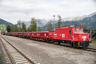 Foto von Bahnschienen, auf dem rechten Gleis steht eine rote Zugmaschine mit Waggons