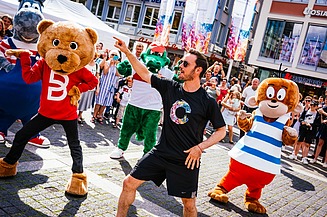 Foto von tanzenden Maskottchen und einem Animator. Drumherum sind viele Menschen.  